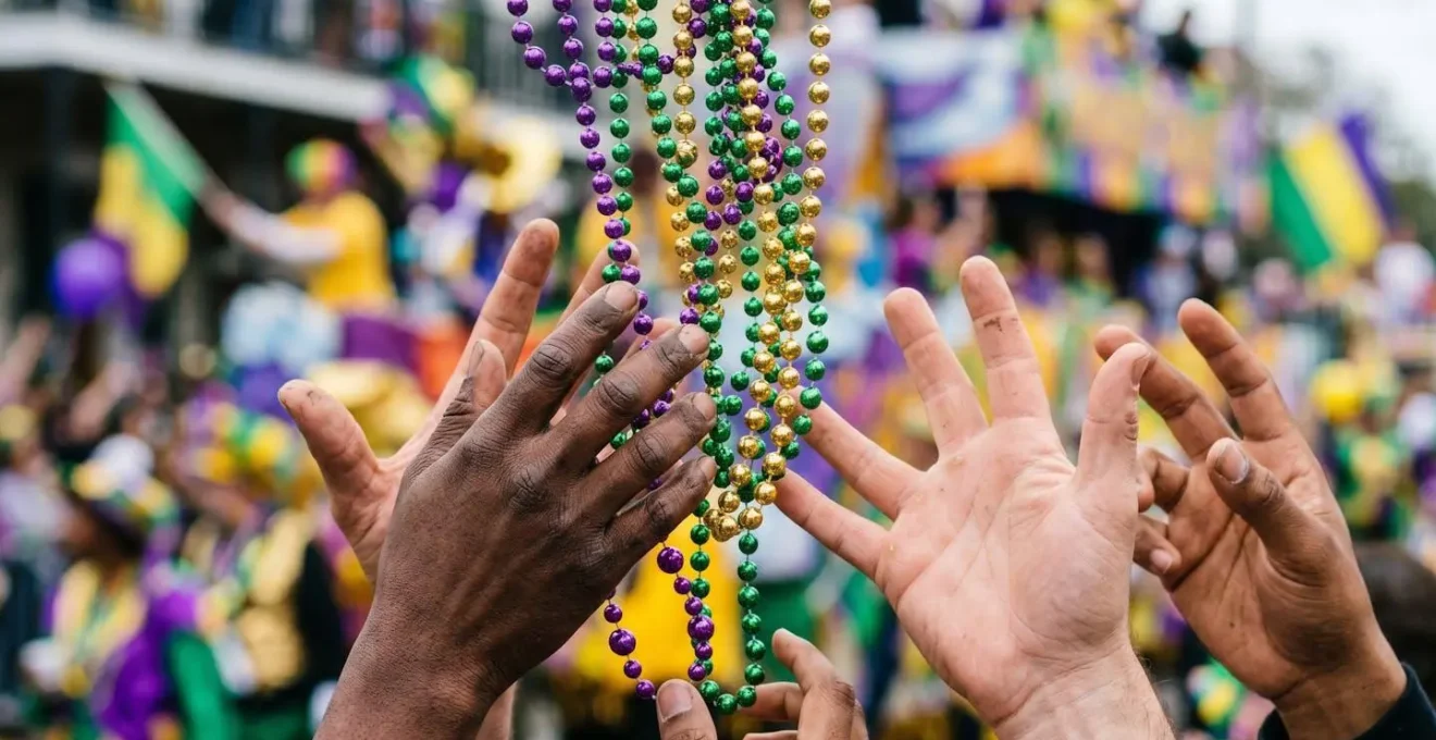 Close-up of hands catching colorful Mardi Gras beads and doubloons from parade float