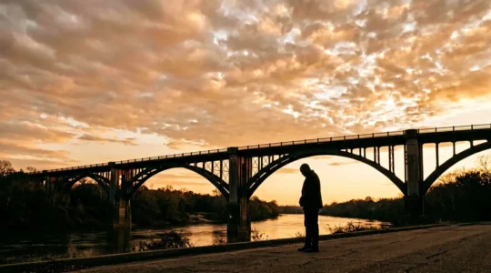 Silhouetted figure standing in contemplation before the Edmund Pettus Bridge at golden hour, capturing the profound reverence required for Civil Rights Trail visitors